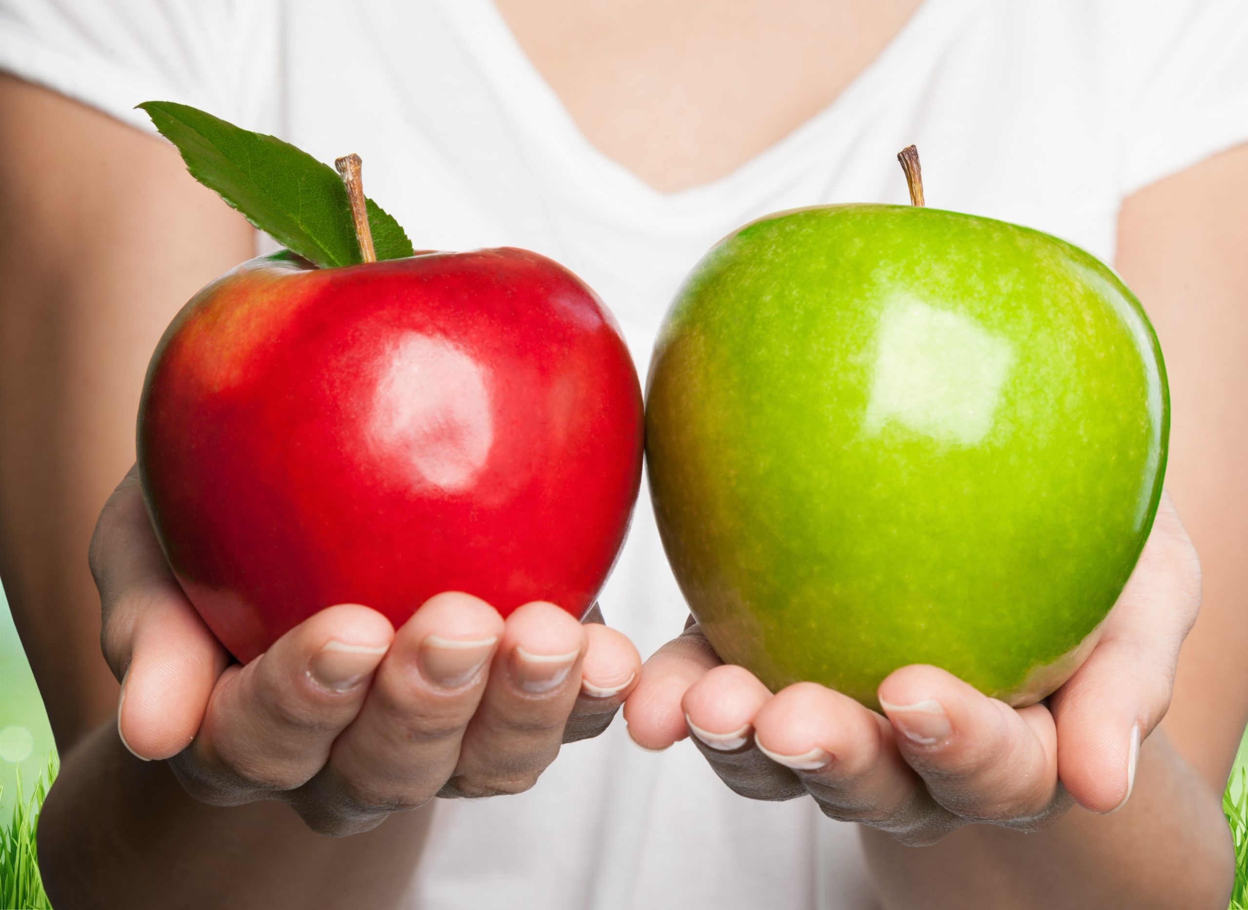 two hands, one holding a red apple and one holding a green apple